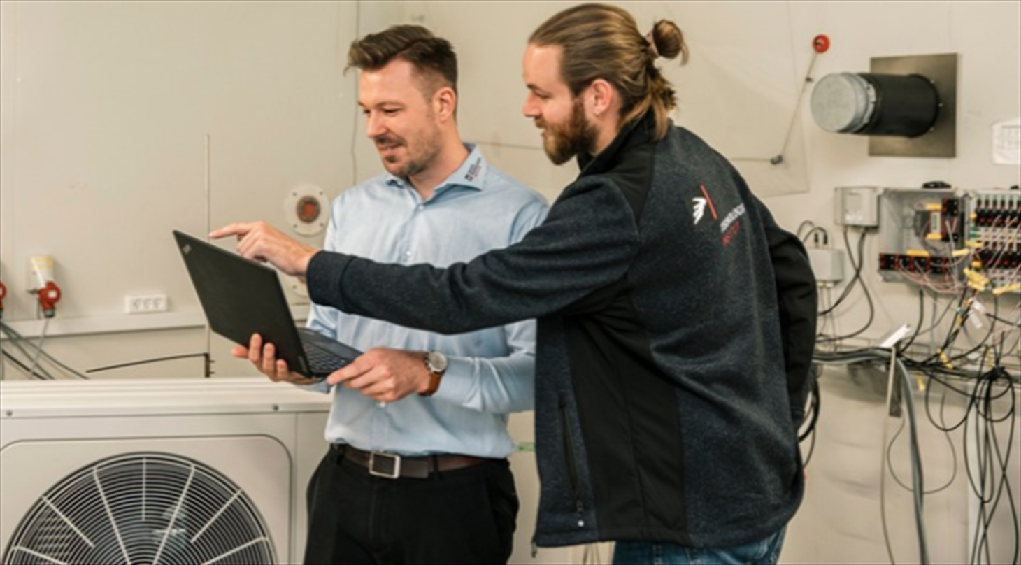 The picture shows two test engineers looking at a computer in front of a heat pump in the Heat Pump Test Laboratory at Danish Technological Institute